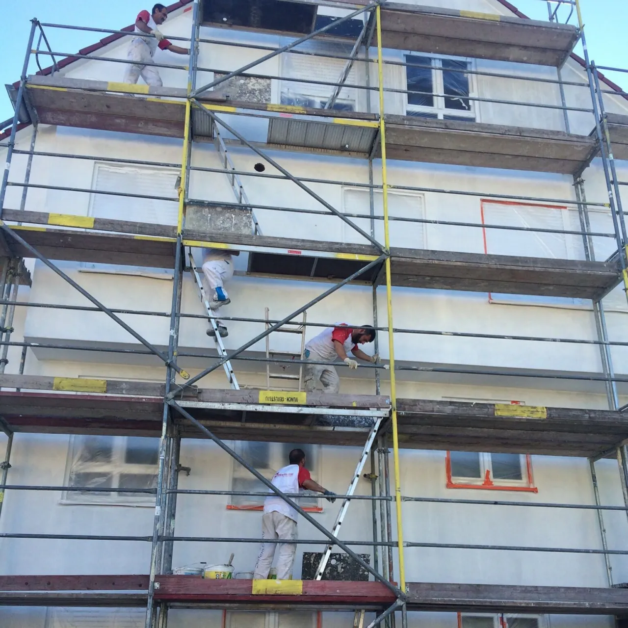 Putzkolonne verputzt die Fassade eines Mehrfamilienhauses vom Gerüst aus