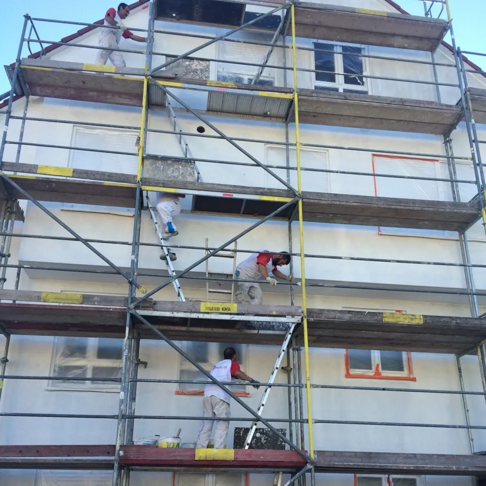 Putzkolonne verputzt die Fassade eines Mehrfamilienhauses vom Gerüst aus