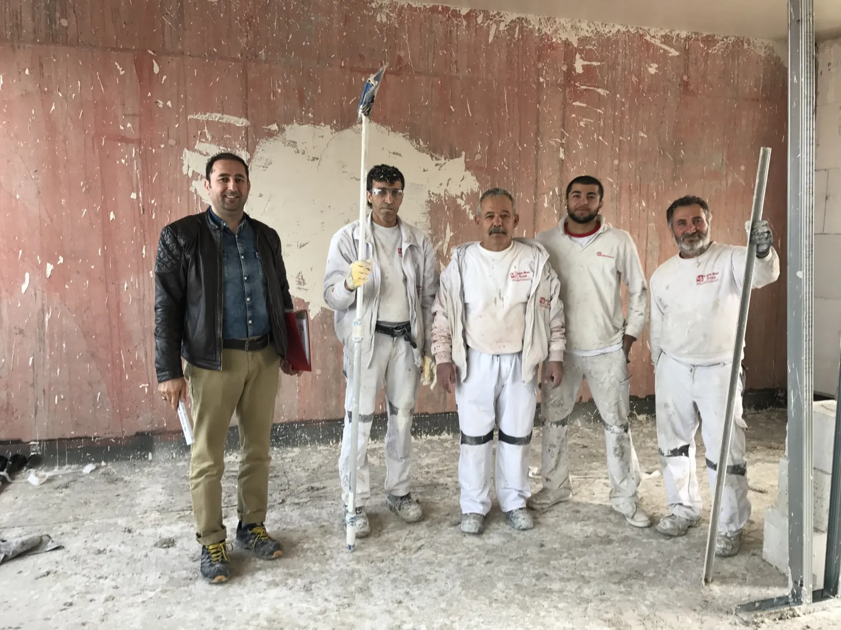 Fünfköpfiges Team von Loga-Bau auf einer Baustelle im Innenausbau, vier davon in weißer Arbeitskleidung